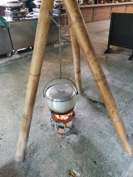 алюминиевый кастрюля с ручкой висит на бамбуковом столбе приготовления пищи на печи глиняный горшок. - Фото, изображение