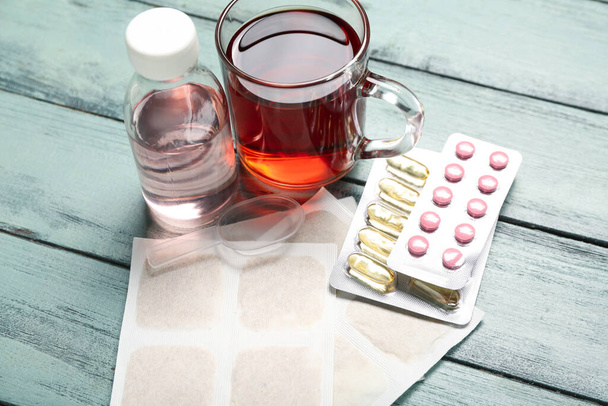 Mustard plasters with cup of tea, pills and cough syrup on color wooden background - Foto, afbeelding