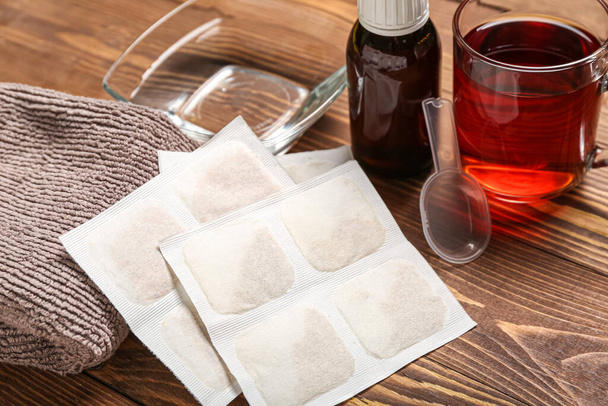 Hořčičné omítky s ručníkem, miskou vody, šálkem čaje a sirupem proti kašli na dřevěném pozadí - Fotografie, Obrázek