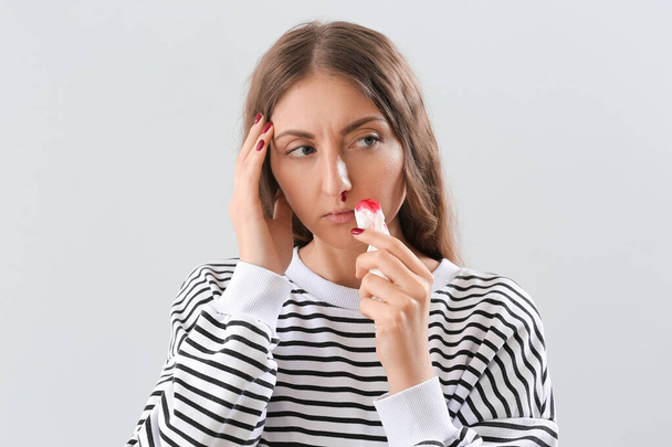 Mujer joven con hemorragia nasal y tejido sobre fondo claro, primer plano - Foto, Imagen