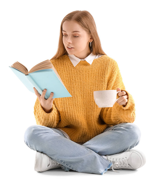 Young woman with cup of hot cocoa reading book on white background - Photo, Image