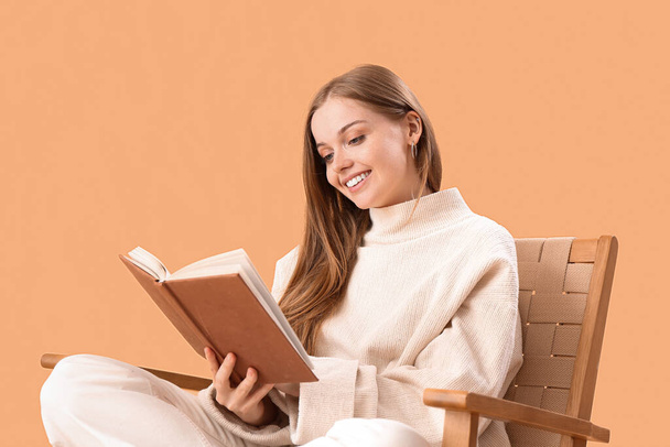 Молода жінка читає книгу в кріслі на бежевому фоні
 - Фото, зображення