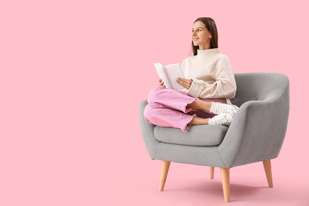 Mooie vrouw met boek zitten in fauteuil op roze achtergrond - Foto, afbeelding