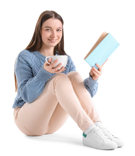 Young woman in blue sweater with cup of cocoa reading book on white background - Photo, Image