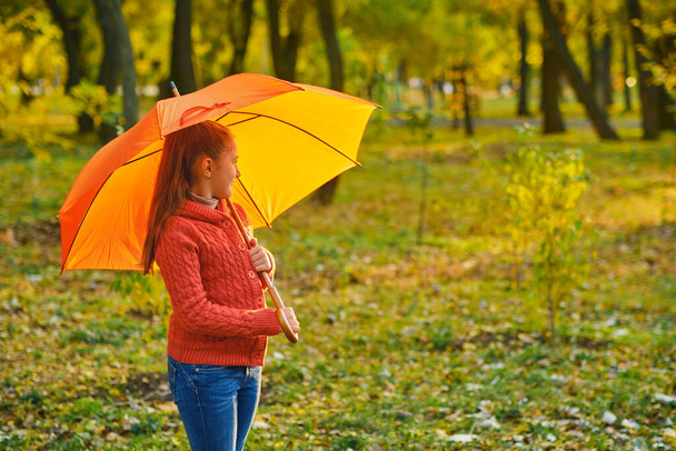 Funny kid under an orange umbrella outdoors in Autumn park - Фото, изображение