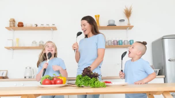 Lachende moeder en dochter en zoon hebben plezier in de moderne keuken in slow motion. Vreugdevolle kinderen en moeder bereiden eten in de keuken. gelukkig familie hebben plezier samen thuis. - Video