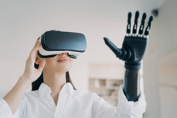 Advertising of bionic prosthetic arm. Modern woman in VR glasses touching virtual objects by high tech robotic artificial limb. Girl using lightweight prosthesis to interact with augmented reality. - Photo, Image