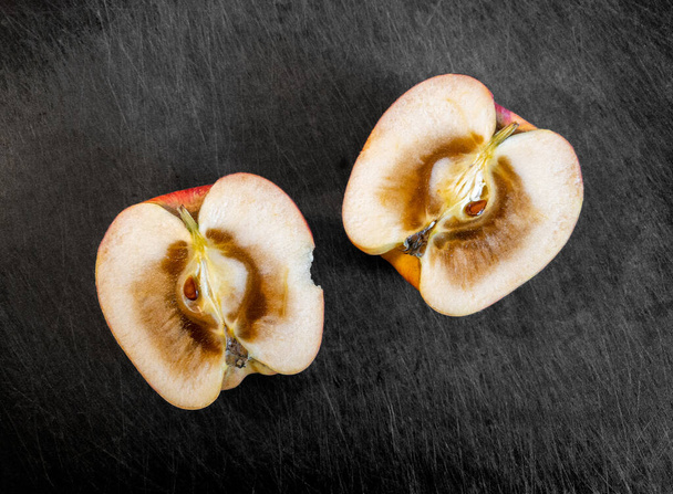 Twee helften van de binnenkant van een open en rotte appel, rustend op een donkere snijplank. - Foto, afbeelding