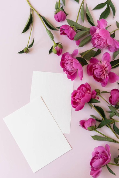 Blank paper invitation cards with copy space. Pink peony flowers bouquet on neutral pastel elegant pink background. Flat lay, top view minimal floral composition - Foto, afbeelding
