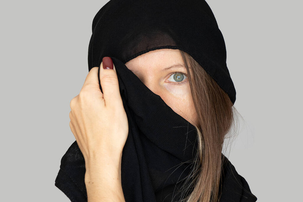 Kız yüzünü ve başını siyah bir eşarpla örtmüş, izole bir arka planda, inanç ve din Müslümandır. - Fotoğraf, Görsel