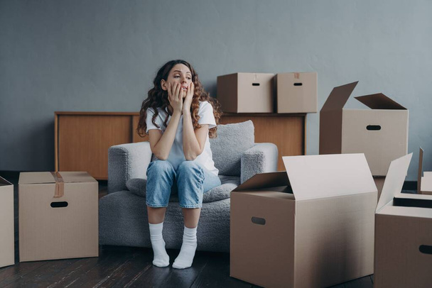 Tired young woman sitting near cardboard boxes on relocation day, having a break during packing things. Upset divorced female starts new life moving out to rented house. Eviction concept. - Фото, изображение