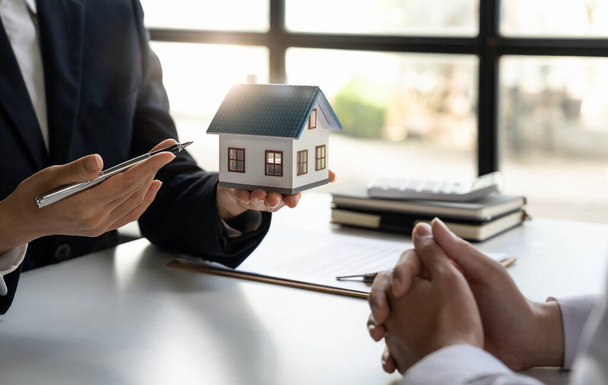 Real estate broker agent presenting and consult to customer to decision making sign insurance form agreement, home model, concerning mortgage loan offer for and house insurance. - 写真・画像