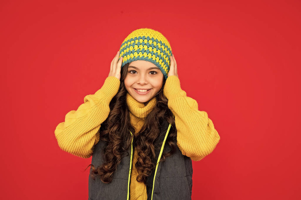 cheerful teen girl on red background. portrait of child wearing warm clothes. express positive emotion. winter fashion. kid with curly hair in hat. - Fotografie, Obrázek