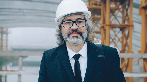 portrait of successful mature man architect wearing safety helmet standing in construction area alone and looking at camera - Fotografie, Obrázek