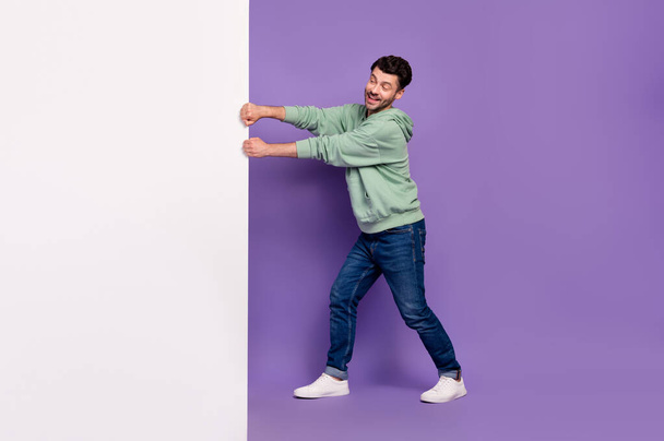 Full length photo of nice young man pulling white wall empty space dressed stylish khaki clothes isolated on purple color background. - Valokuva, kuva