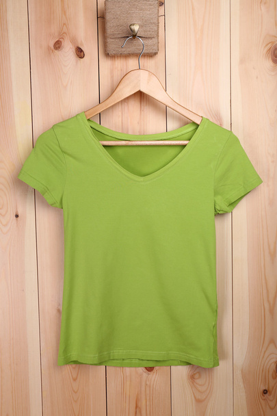 Female t-shirt on hanger on wooden wall background - Foto, immagini