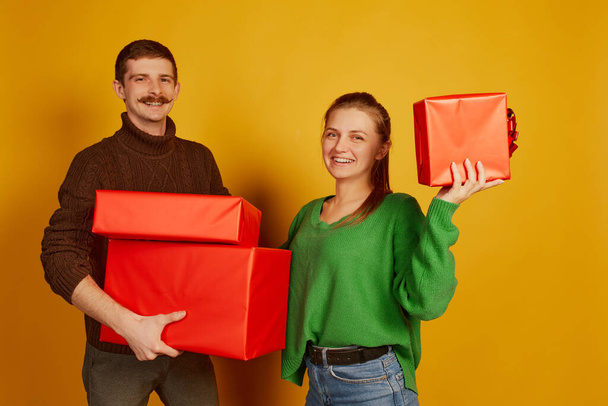 Portrait of cheerful young people, man and woman holding big present boxes isolated over yellow background. Concept of holidays, happiness, emotions, facial expression, joy, celebration - Photo, Image
