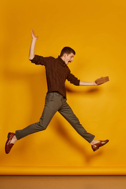 Portrait of young cheerful man jumping in joy with present box isolated over yellow studio background . Happy. Concept of holidays, happiness, emotions, facial expression, joy, celebration - Fotografie, Obrázek