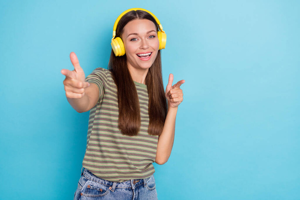 Portrait photo of young attractive nice gorgeous woman wear striped khaki t-shirt toothy excited fingers pick you listen earphones isolated on blue color background. - Valokuva, kuva
