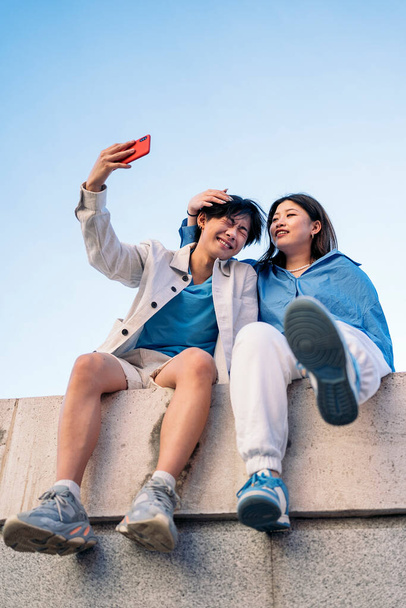 Cool and young asian couple sitting in the city posing and taking selfie with their phone. - Fotografie, Obrázek