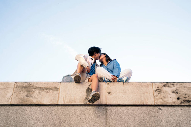 Viileä ja nuori aasialainen pari istuu Madridissa ja suutelee. - Valokuva, kuva