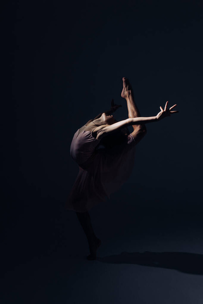 Pembe elbiseli balerin kız dans eder ışıkla aydınlatılır karanlık arka planda. - Fotoğraf, Görsel