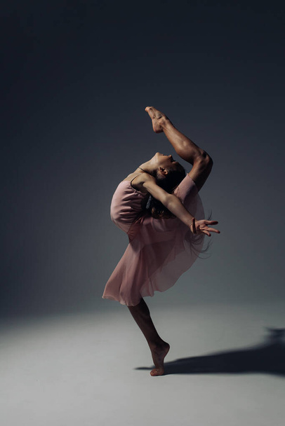 Ballerina bambina in abito rosa danza illuminata dalla luce su sfondo scuro. - Foto, immagini