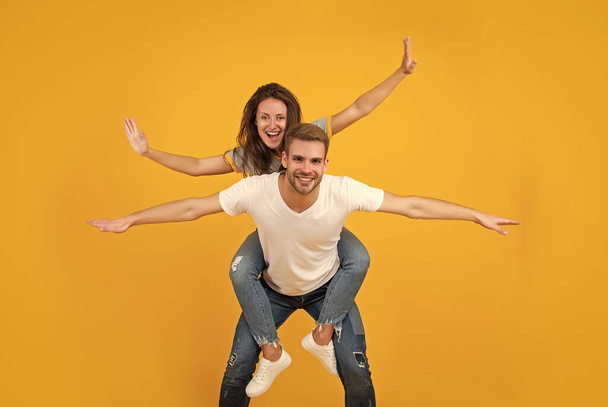 Happy couple in love of girl and man pretend flying doing piggyback ride yellow background, playful. - Fotoğraf, Görsel