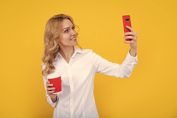 Kahveli neşeli sarışın kadın sarı arka planda telefonla selfie çekiyor.. - Fotoğraf, Görsel