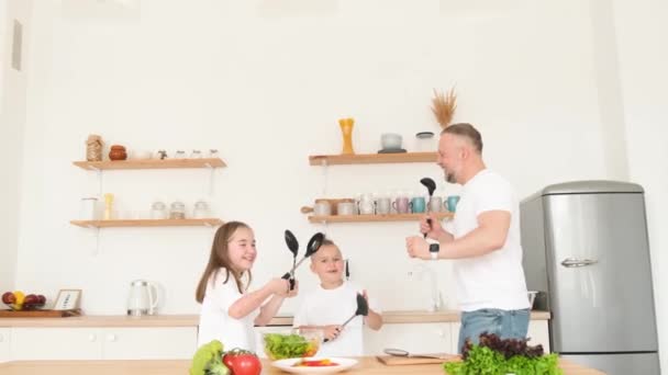 Сумасшедший отец танцует и поет со своими детьми на кухне. Счастливая семья отдыхает на кухне. 4k видео - Кадры, видео