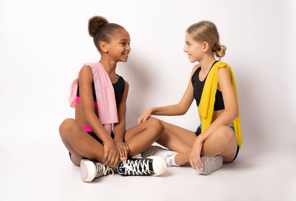 Two charming girls gymnasts in sports clothes sitting on floor over white background. - Foto, Imagen