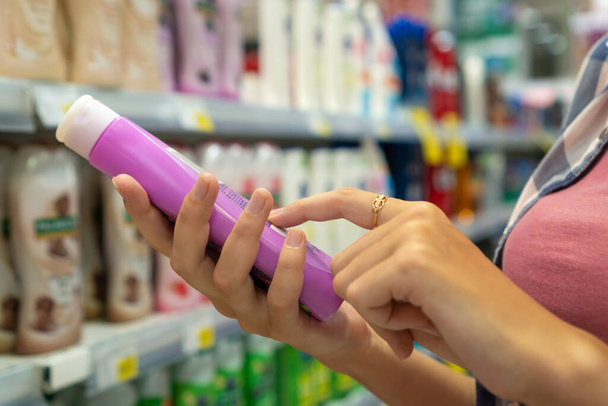 Dükkandaki bir şişe duş jeli hakkında bilgi okuyan genç bir kadının ellerinin yakın çekimi. Mağazadan kozmetik ürünleri almak. Alışveriş gezisi. - Fotoğraf, Görsel