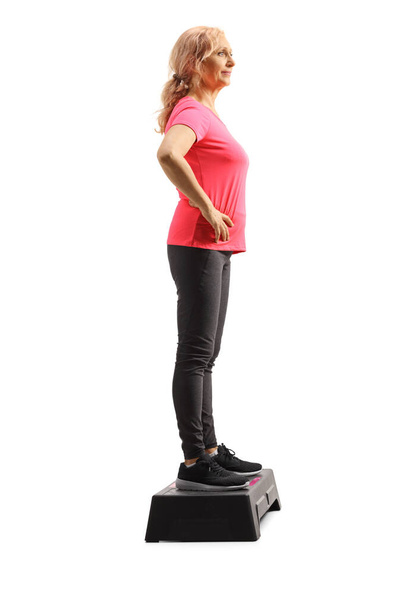 Full length profile shot of a mature woman standing on an aerobic stepper isolated on white background - Foto, immagini