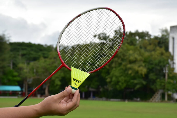 Raqueta de bádminton y lanzaderas de bádminton tomados de la mano para jugar al aire libre, enfoque suave y selectivo en cuerdas y raquetas, concepto para actividades al aire libre. - Foto, imagen