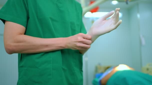Portret azjatyckiego chirurga w masce medycznej stojącego i noszącego rękawiczki medyczne na sali operacyjnej w szpitalu. Zespół profesjonalnych chirurgów. Opieka zdrowotna, koncepcja ratownictwa medycznego - Materiał filmowy, wideo