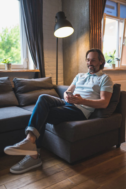 Connected. Bearded man sitting in the armchair awith a smartphone in hand - Foto, Imagem