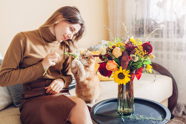 Frau spielt mit Ingwer Katze macht Blumenstrauß in Vase auf dem Tisch gestellt. Neugieriges Haustier, das zu Hause Spaß hat. Gemütliches Ambiente - Foto, Bild