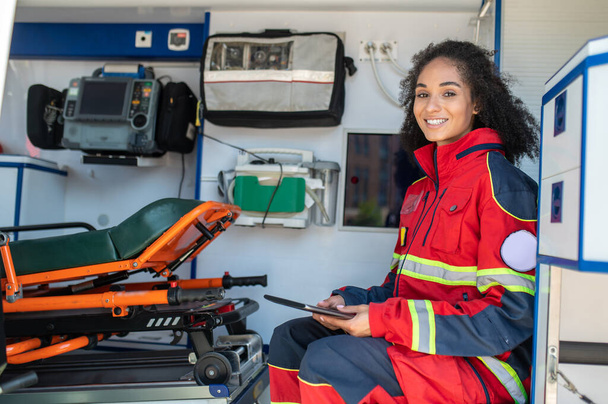 Smiling happy paramedic with the tablet in her hands sitting in the medical emergency vehicle - Fotografie, Obrázek