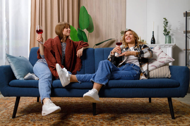 Madre e figlia spettegolano mentre bevono vino mentre sono seduti sul divano di casa - Foto, immagini