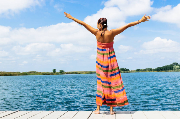 Vista posteriore di donna felice godendo in libertà mentre in piedi su un molo con le braccia tese durante le vacanze estive.  - Foto, immagini