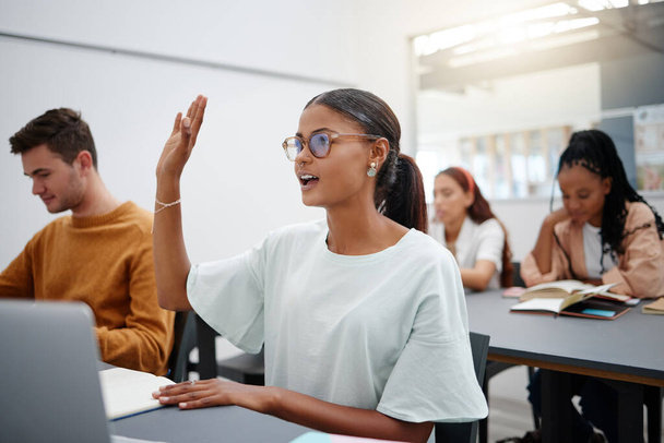 Education through questions by students at university with diversity during lecture. Young woman in classroom, asking with hand up while classmate listen on. Motivation through discussion - Photo, Image