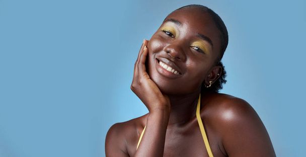 Black woman, smile and makeup in mockup for skincare beauty and cosmetics against blue backdrop. Model, happy and hand on face, for skin wellness and health in portrait against studio background. - Foto, immagini