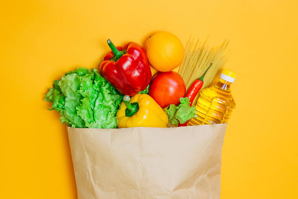Red, yellow pepper, chili, sunflower oil, tomato, orange, pasta, lettuce in paper craft package, a set of vegetarian food on an orange background, top view, flat lay - 写真・画像