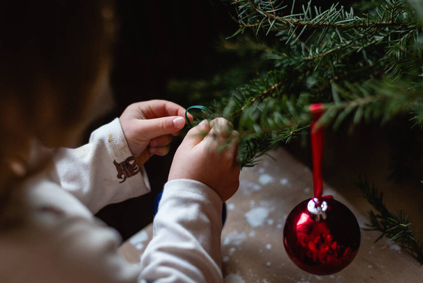 Vista cercana de las manos de los niños decorando el árbol de Navidad en casa durante el día - Foto, Imagen