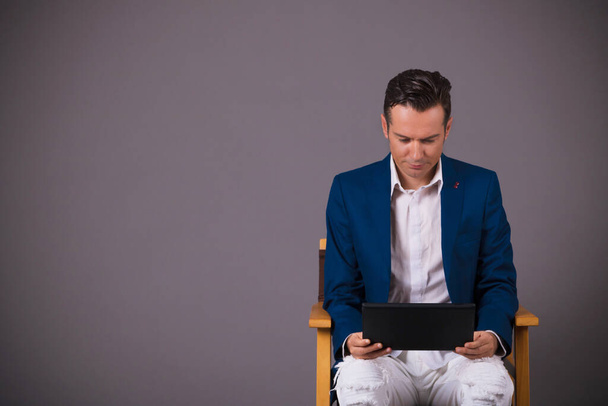 Lächelnder Geschäftsmann beim Surfen im Netz auf dem Touchpad, während er vor grauem Hintergrund sitzt. Kopierraum  - Foto, Bild