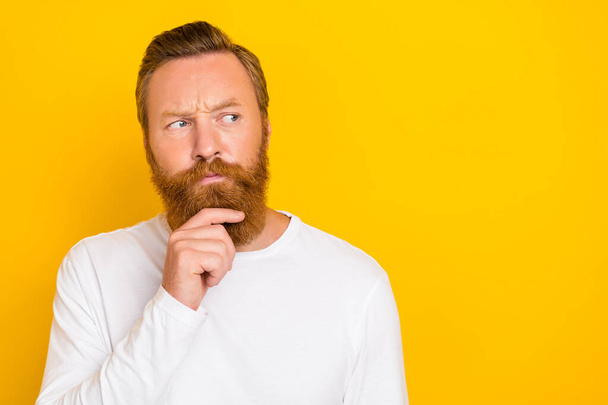 Photo portrait of attractive young man touch chin thoughtful look empty space wear stylish white outfit isolated on yellow color background. - 写真・画像