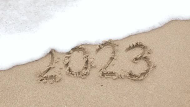 2022 рука написать цифры на песчаном пляже для счастливого Нового 2023 года, Морская волна смывает числовой рукой написано на золотом пляже песчаного моря. Прощай, 2022 год - Кадры, видео