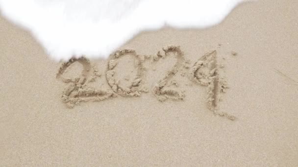 2024 χέρι γράψει στοιχεία για την αμμώδη παραλία για Ευτυχισμένο το Νέο Έτος 2025, Το κύμα της θάλασσας ξεπλένει τον αριθμό χέρι γραμμένο στη χρυσή άμμο παραλία θάλασσα. Αντίο 2024. - Πλάνα, βίντεο