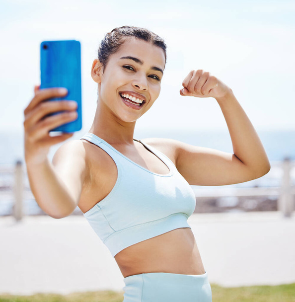 Phone selfie, fitness girl flexing arms, happy smile for workout, exercise or training by beach. Exercise, training or sports health influencer woman for wellness motivation for 5g social media post. - Фото, зображення