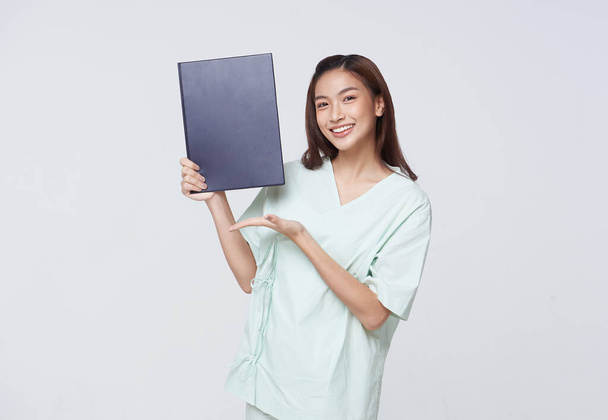 Asian teenage woman wearing a patient gown holding a policy book for assurance in life with a smiling face, insurance concept. - Photo, Image